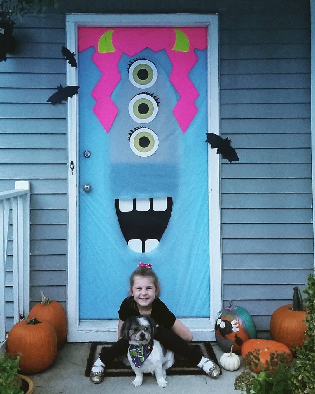 Blue door decorated as a three-eyed monster with a girl and dog sitting nearby.
