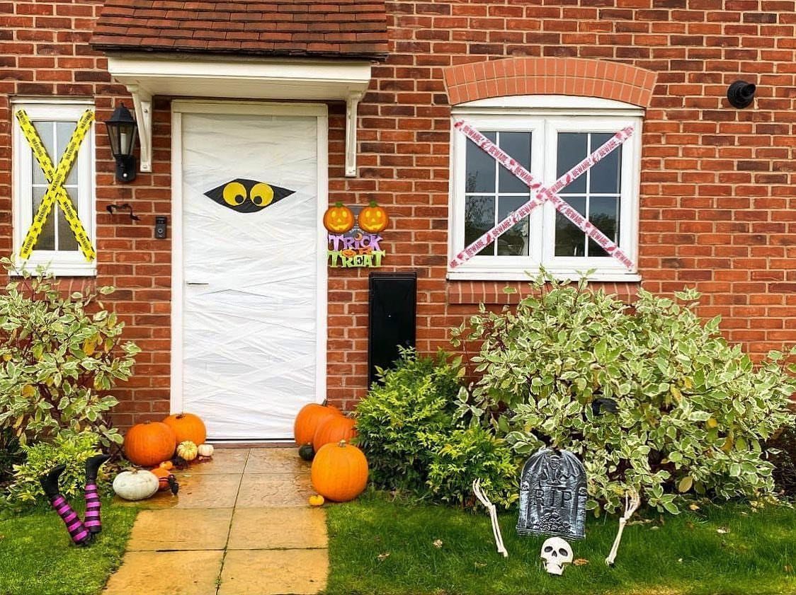 Mummy wrapped front door with yellow eyes, pumpkins, and a skull tombstone.