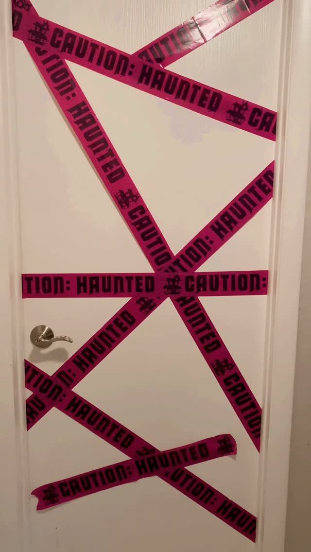 White door decorated with pink haunted caution tape in a crisscross pattern