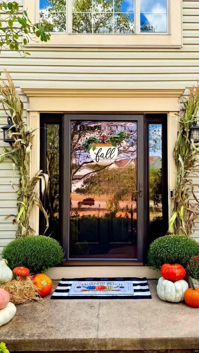 Front door decorated with pumpkins, corn stalks, and a Fall sign for autumn.