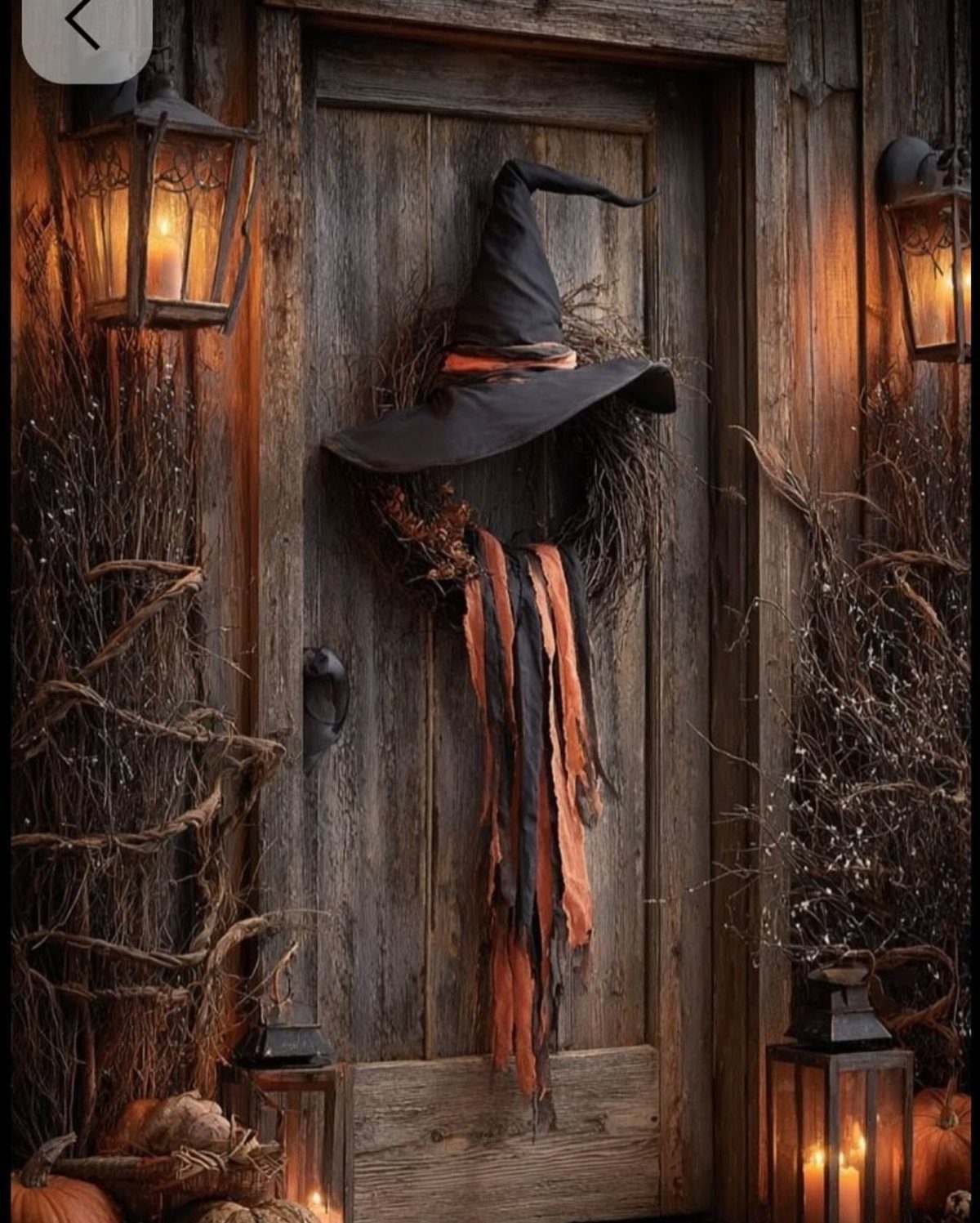 Rustic wooden door decorated with a black witch hat and glowing lanterns