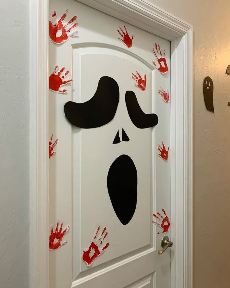 White door decorated with a black screaming ghost face and red paper handprints.