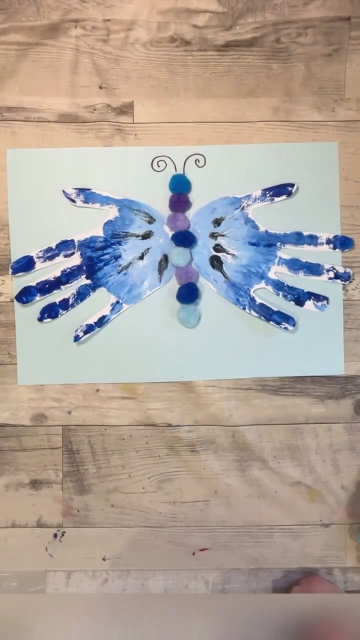Blue paint handprint butterfly craft on light blue paper over a wooden background