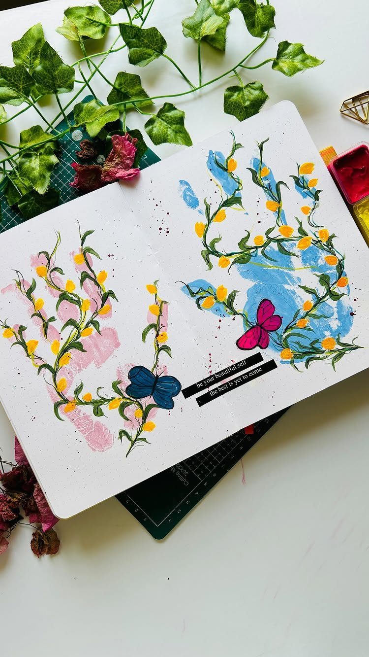 Handprint flowers in pink and blue with yellow petals in an open sketchbook.