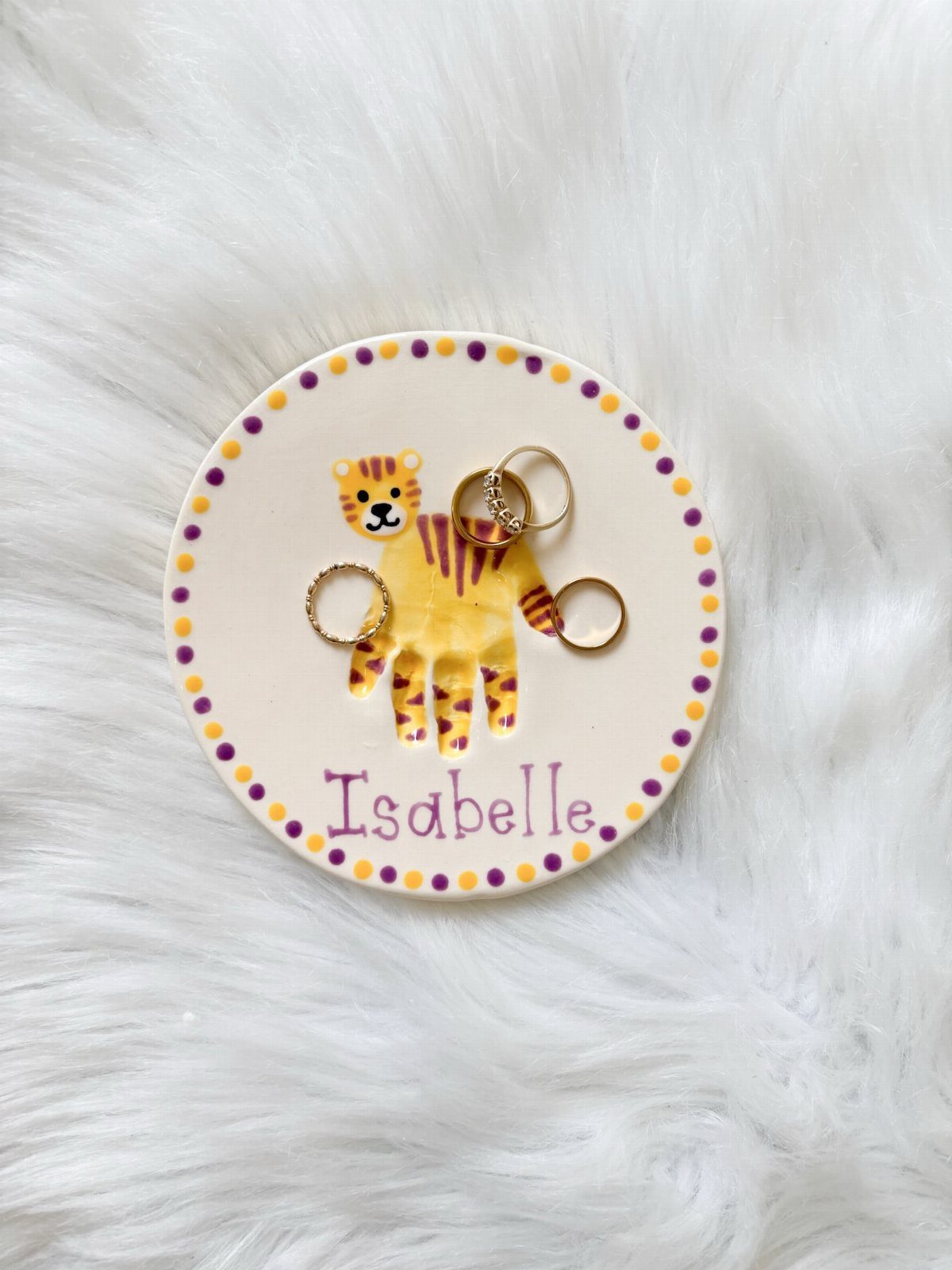 Ceramic jewelry dish with a yellow handprint tiger and gold rings on white fur