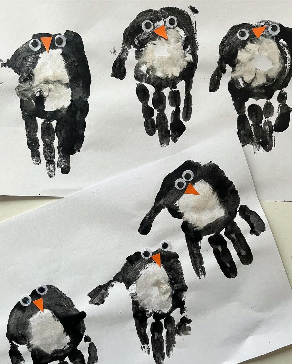 Penguin figures made from black and white paint handprints on white paper.