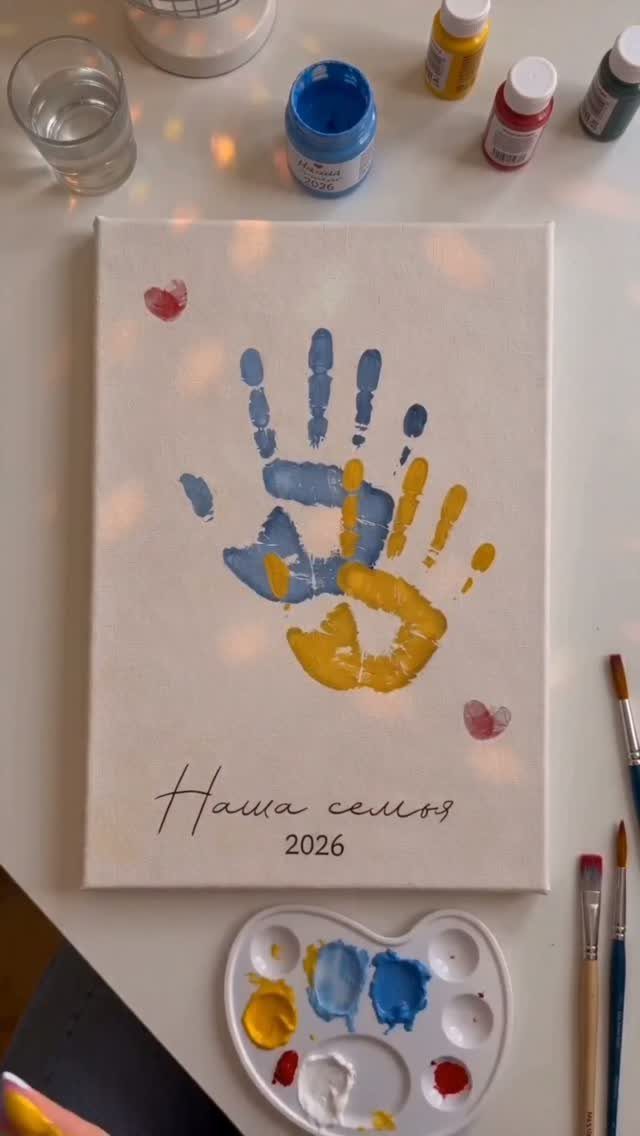 Overlapping blue and yellow handprints on a white canvas with paint supplies around.