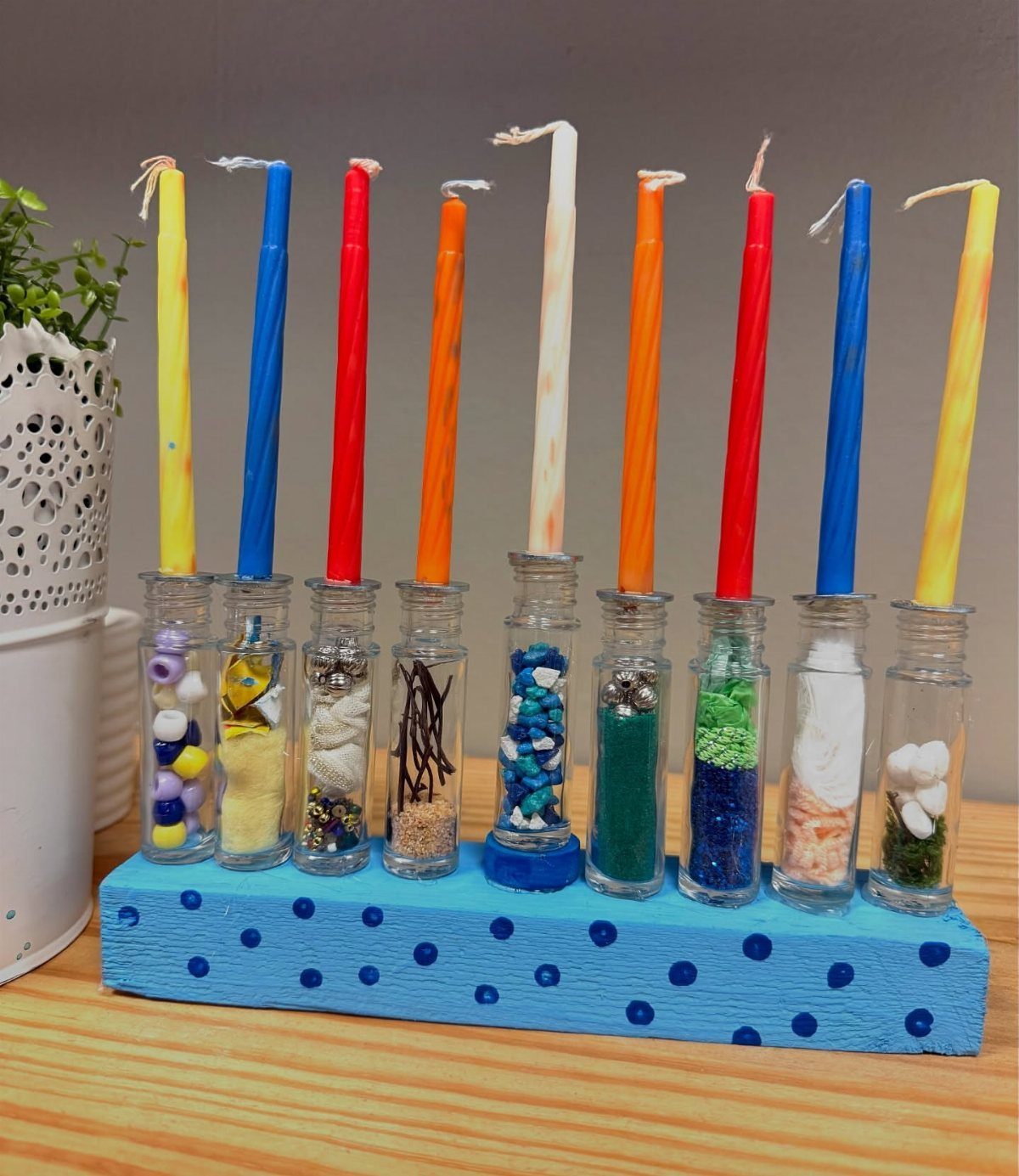 Handmade menorah with colorful candles in glass vials on a blue polka-dot base