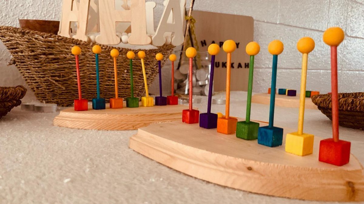 Colorful wooden menorahs with painted pegs on light wood bases in a festive setting