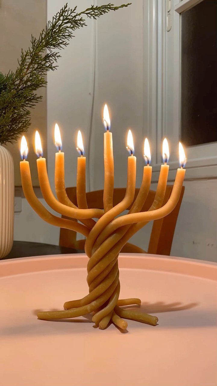 Handmade menorah made of twisted yellow candles with nine lit flames on pink surface
