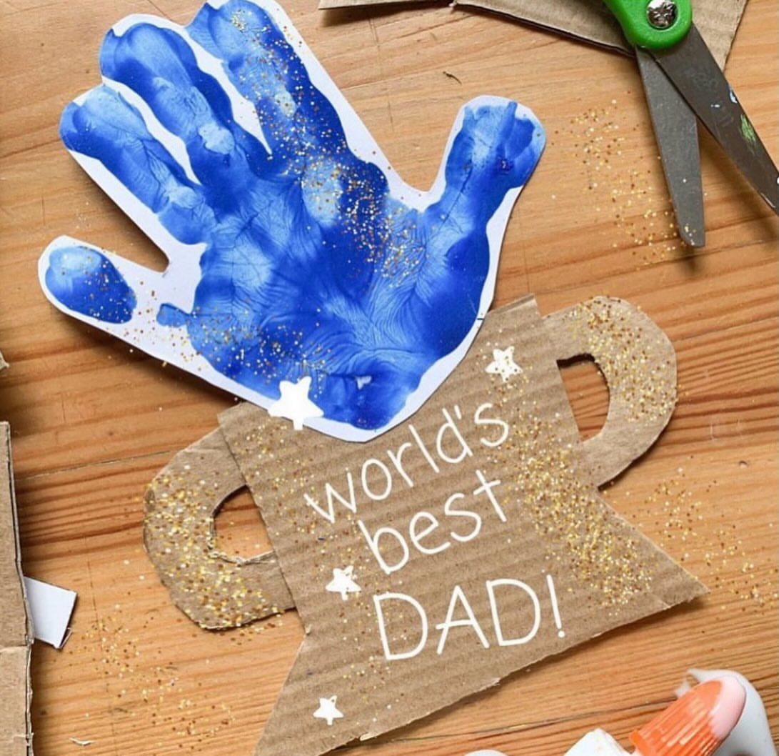 Handmade Father's Day card with a blue handprint and cardboard mug on wood.