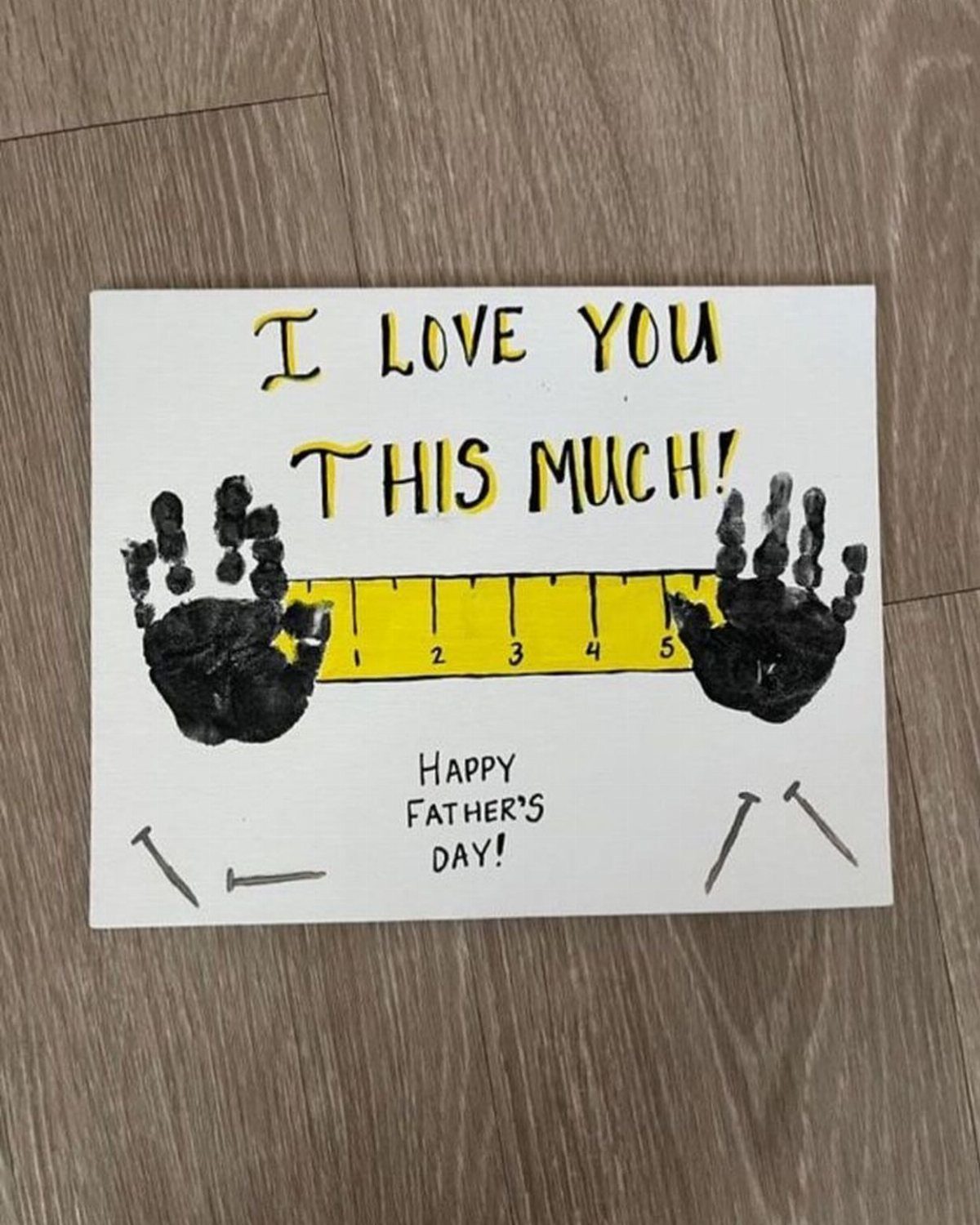 Handmade Father's Day card with black handprints and a yellow ruler on wood.
