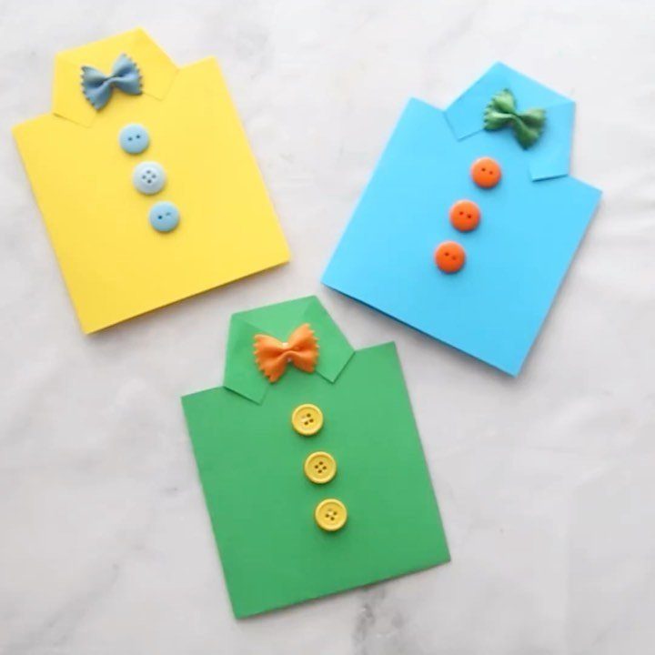 Three colorful handmade shirt-shaped cards with bow ties and buttons on white marble.