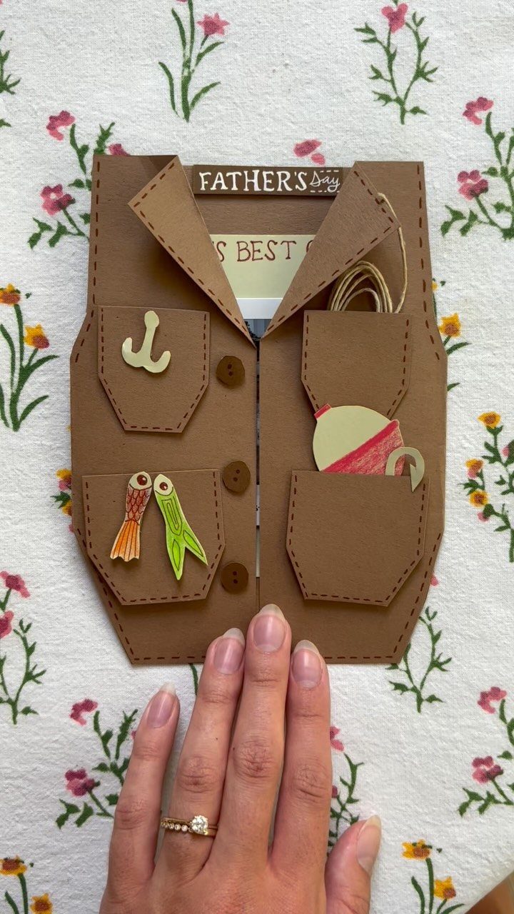Brown cardstock fishing vest craft with paper lures and hook on floral fabric