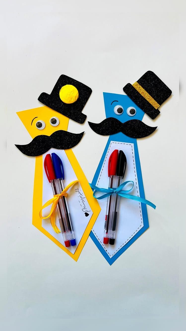Two colorful paper tie crafts with mustaches and top hats holding pens.