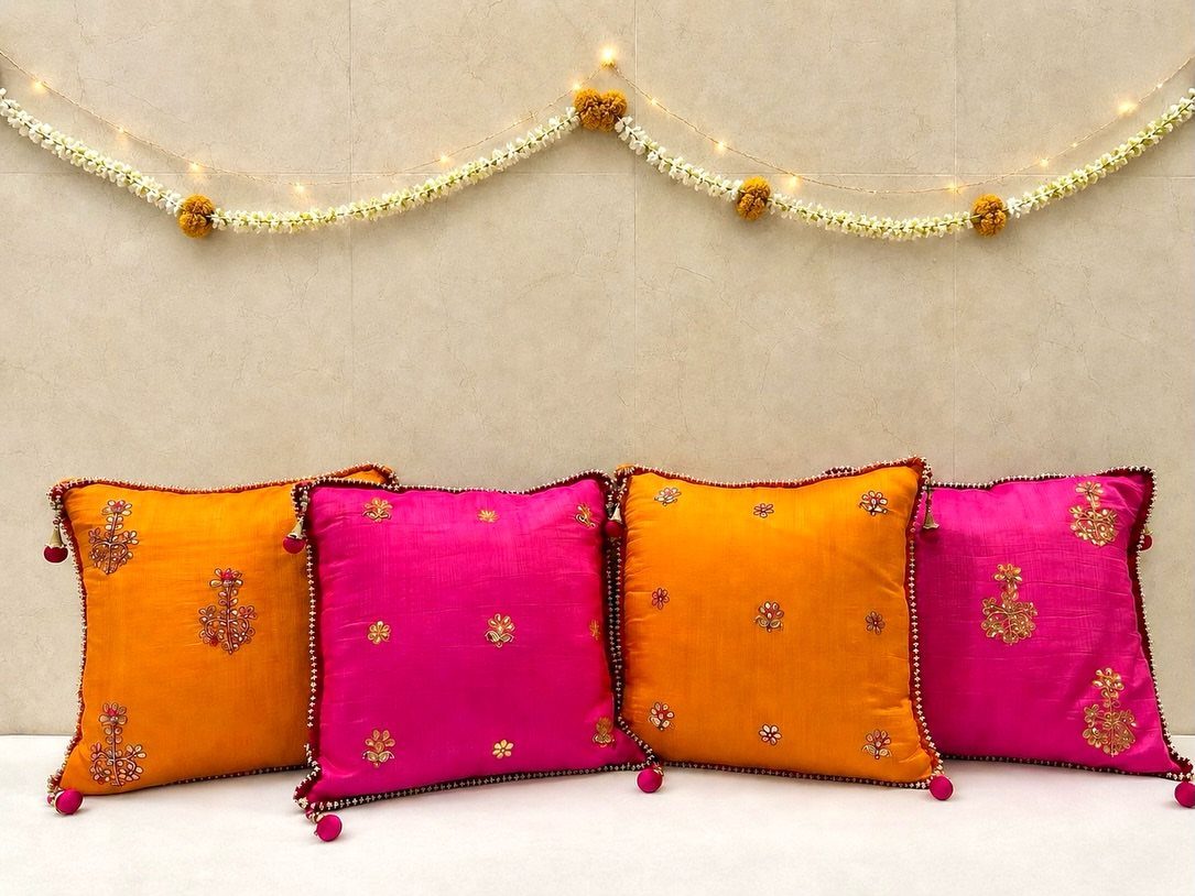 Bright orange and pink festive cushion covers with gold embroidery and pom-pom tassels.