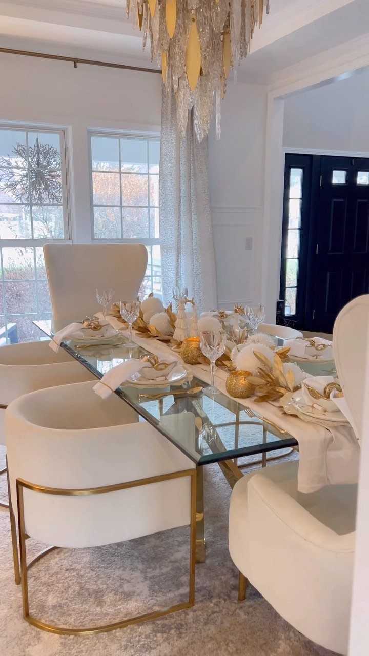 Festive dining table with gold and white decor, glass top, and gold chandelier.