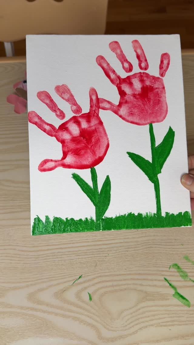 Red handprint flowers with green stems painted on a white canvas background.