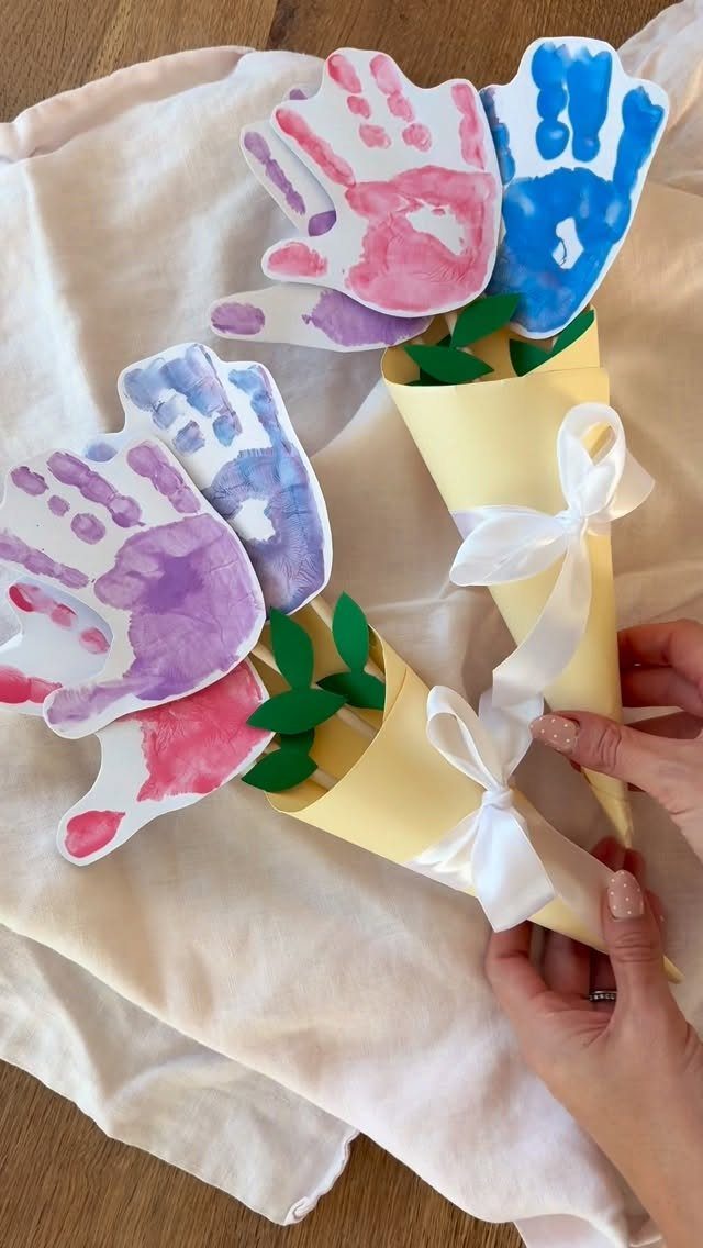 Handprint flower bouquets in yellow paper cones tied with white ribbons on white fabric.