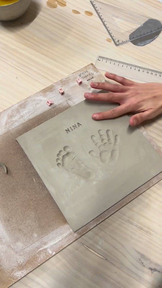 Clay slab with baby handprint and footprint impressions and the name NINA stamped.