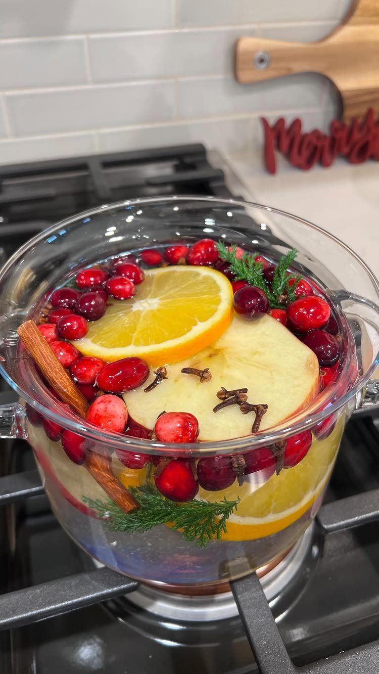 Simmering potpourri with orange, apple, and cranberries in a glass pot on stove.