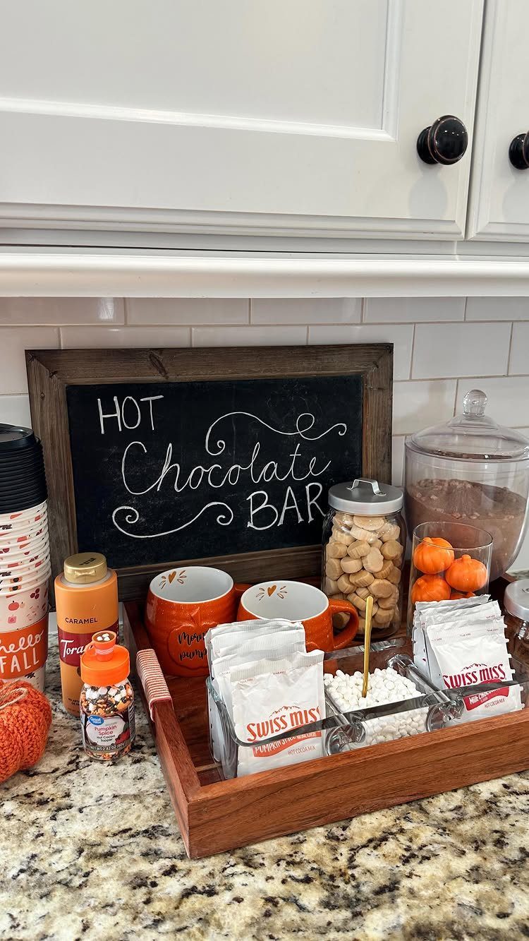 Hot chocolate bar with orange mugs, cocoa packets, and toppings on a wooden tray.