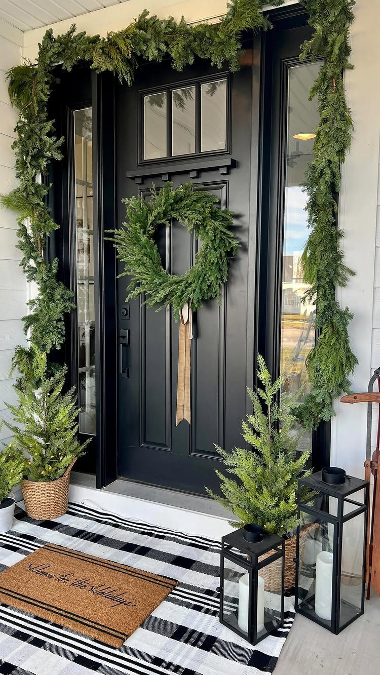 Black front door adorned with a green evergreen wreath and matching greenery garland.