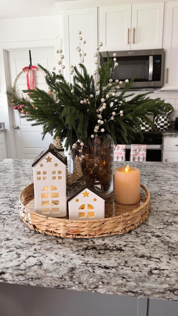 Winter centerpiece with evergreen branches, white ceramic houses, and a lit candle on a tray.
