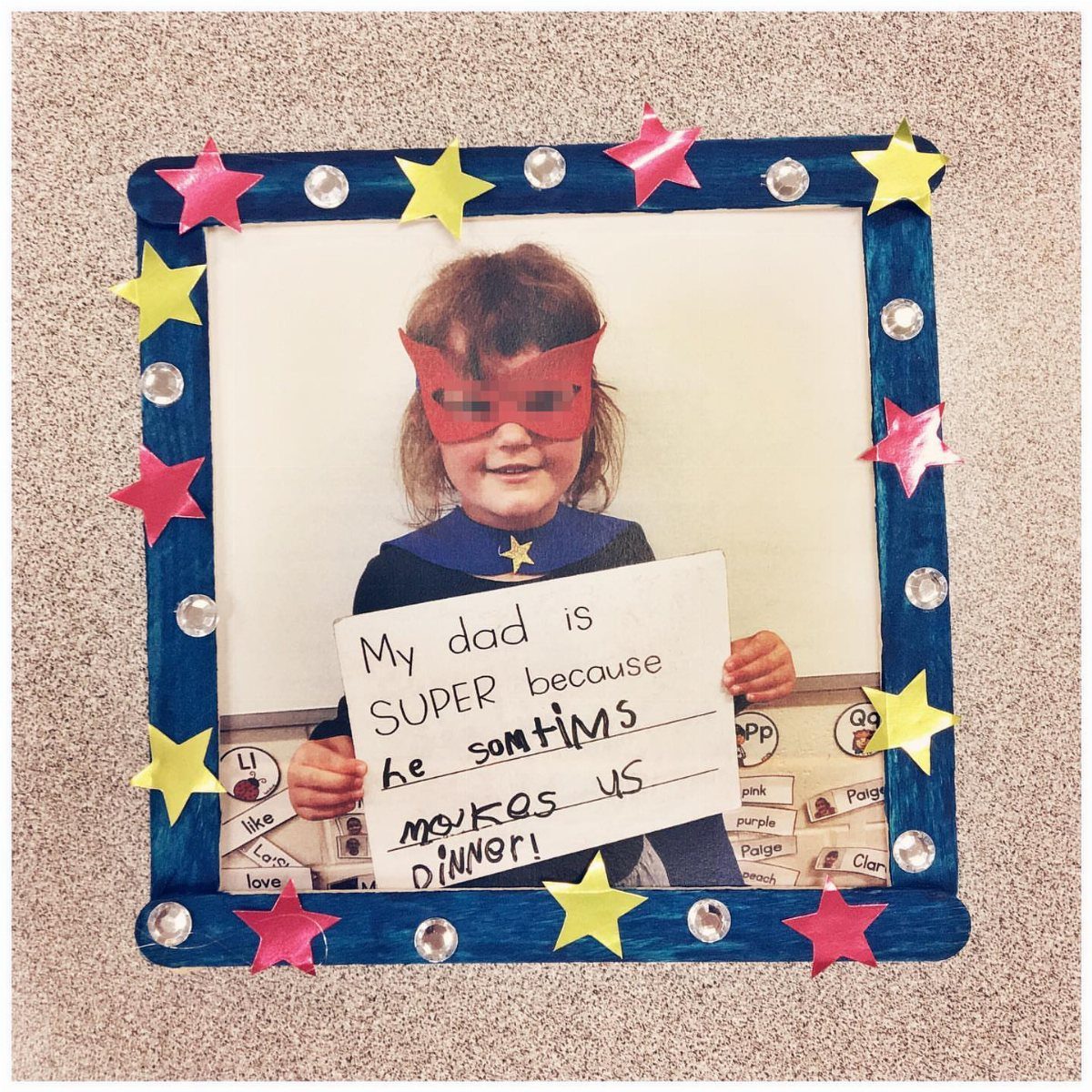 Child in superhero costume holding a sign about their dad in a star-decorated frame