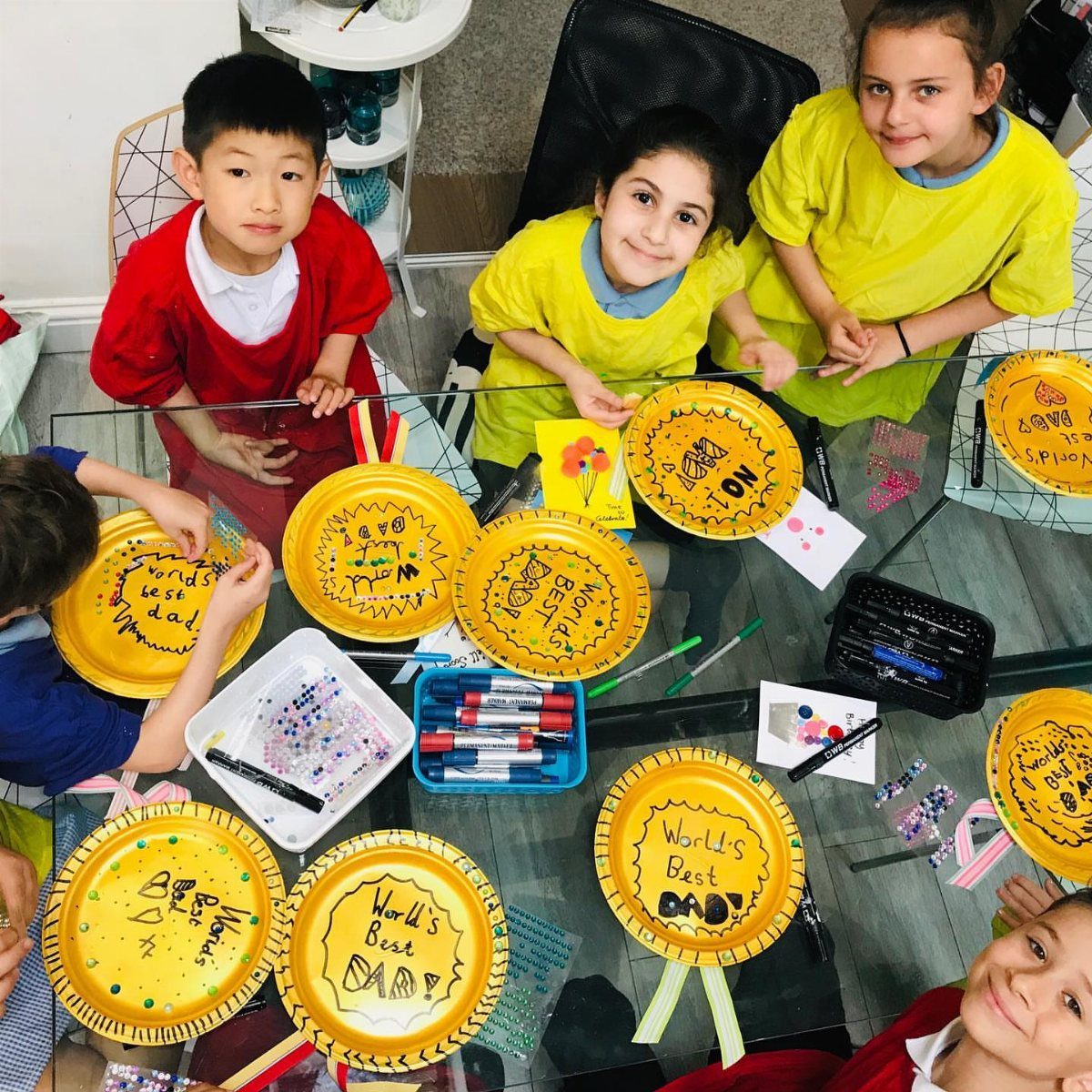 Children sitting around a table with handmade yellow Father's Day plate crafts.