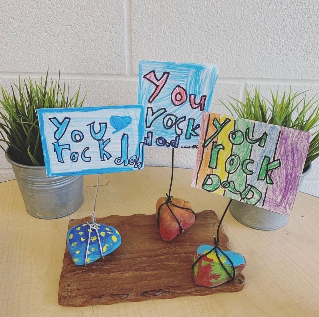 Painted rocks holding hand-drawn signs that say You rock dad on wooden slab