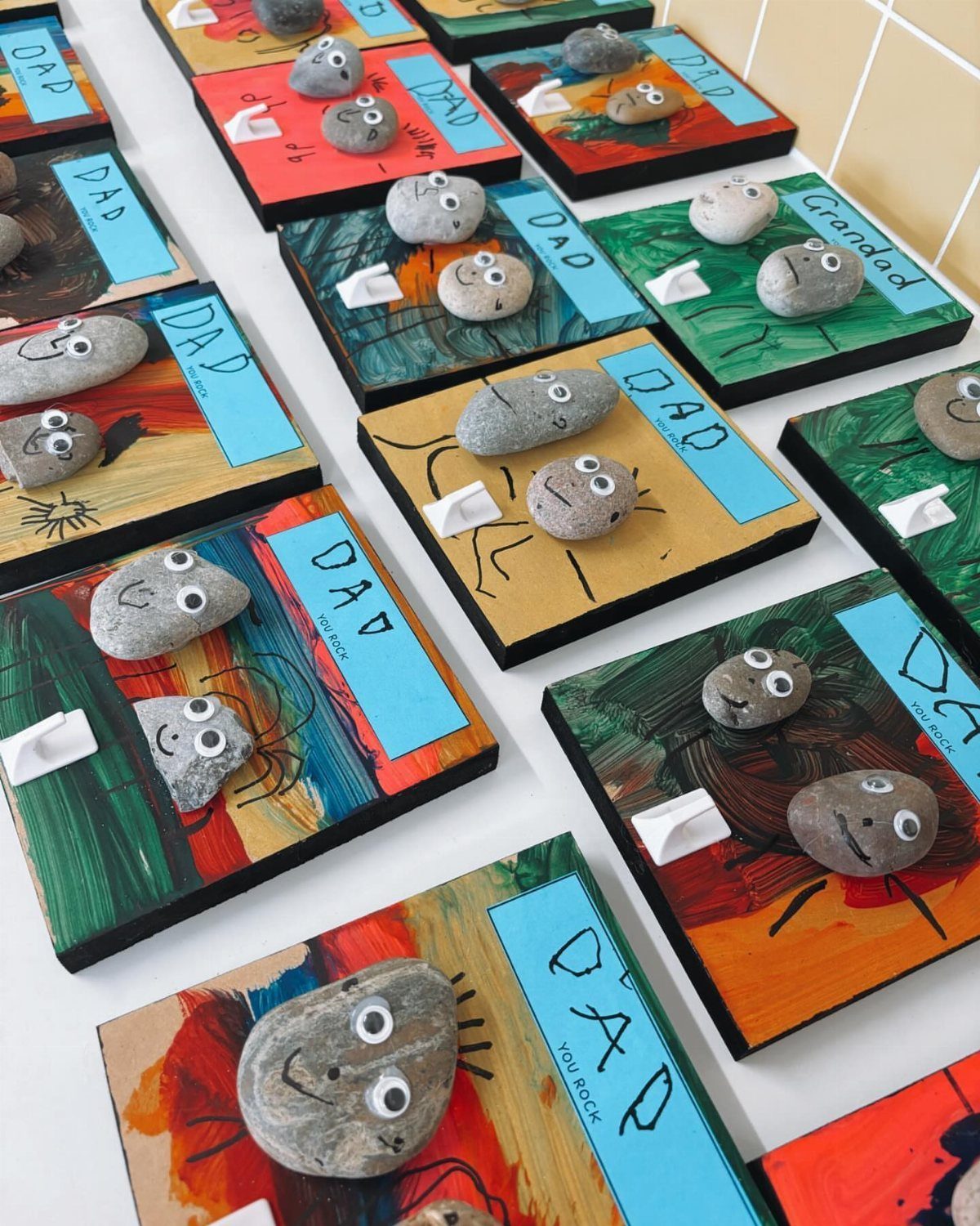 Painted wooden squares with googly-eyed stones and blue labels saying Dad You Rock