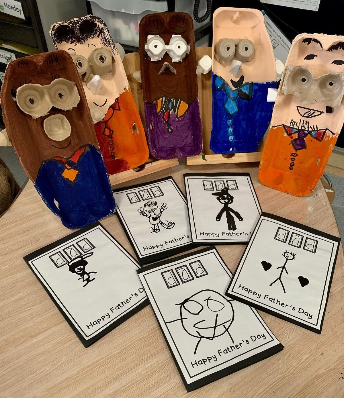 Painted egg carton figures and hand-drawn Father's Day cards on a wooden table.