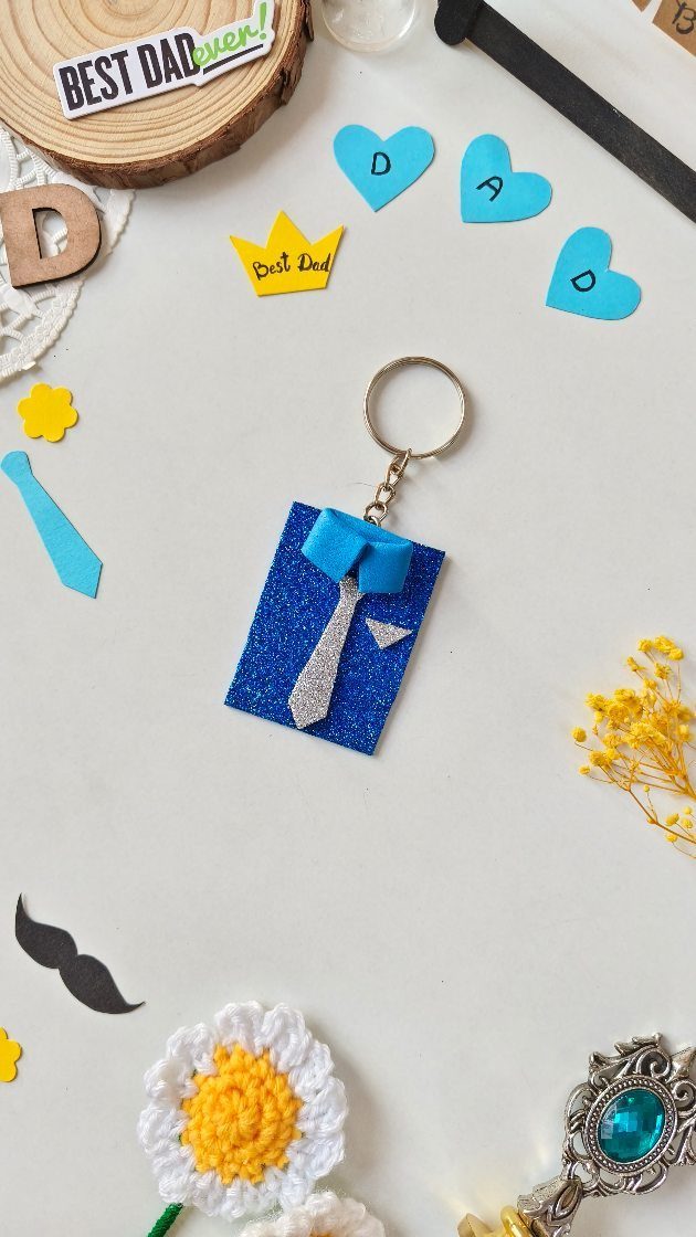 Handmade blue glittery tie keychain surrounded by Father's Day themed craft decorations.