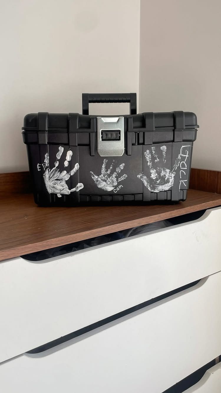 Black plastic toolbox decorated with white handprints sitting on a wooden dresser.