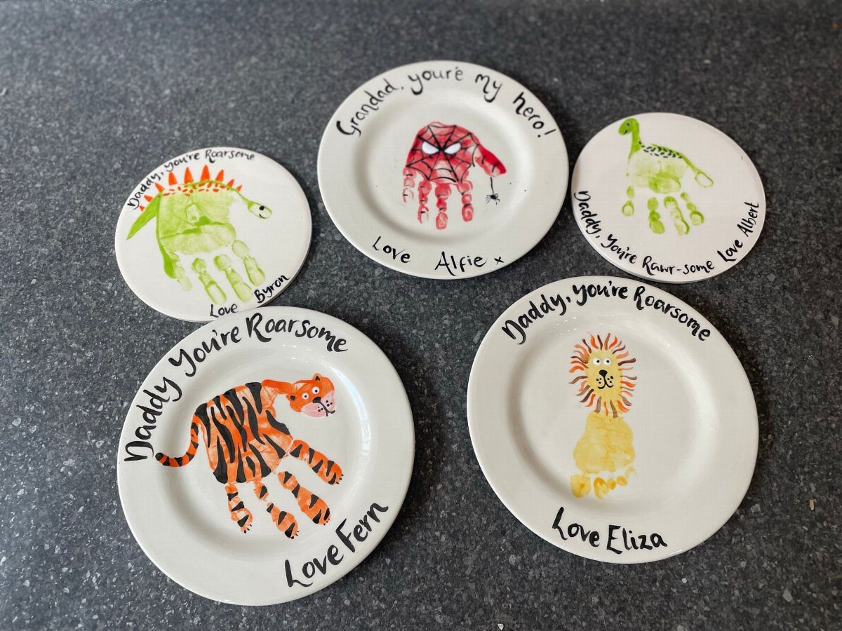 Five white ceramic plates with colorful handprint animal paintings and handwritten Father's Day messages.