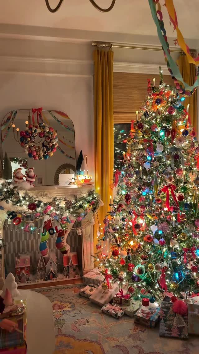 Christmas tree with multicolored lights and ornaments next to a decorated fireplace mantel.