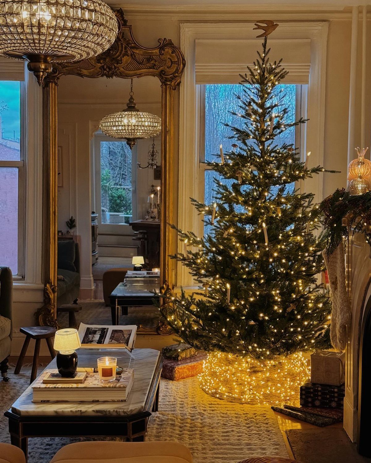 Christmas tree with warm lights in a living room with gold mirror and chandelier