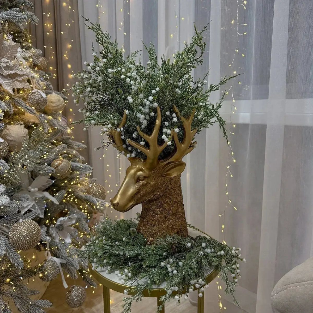 Gold deer head sculpture with pine branches and white berries near a Christmas tree