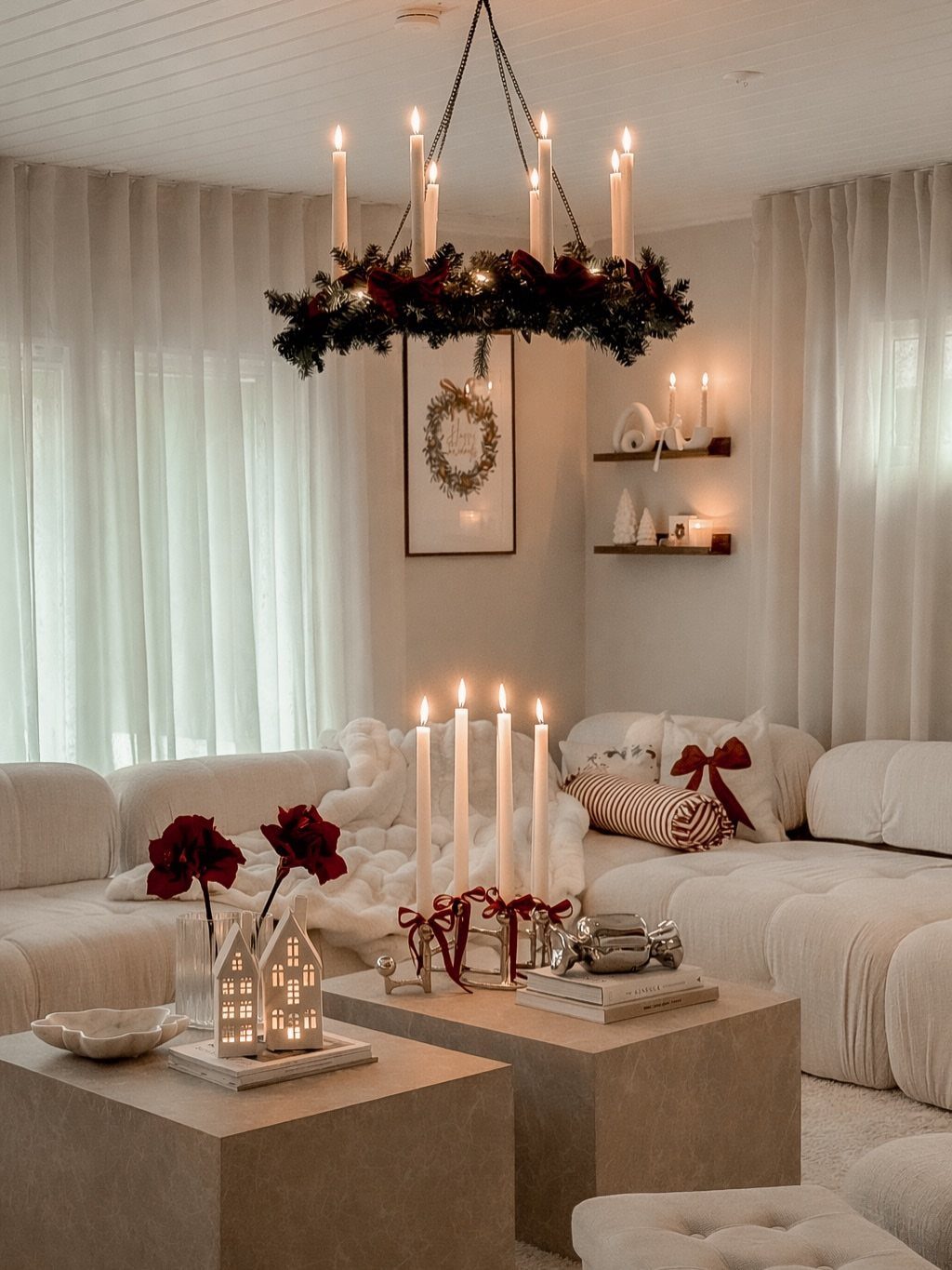 White living room with Christmas decor, candle chandelier, and red bow pillows.