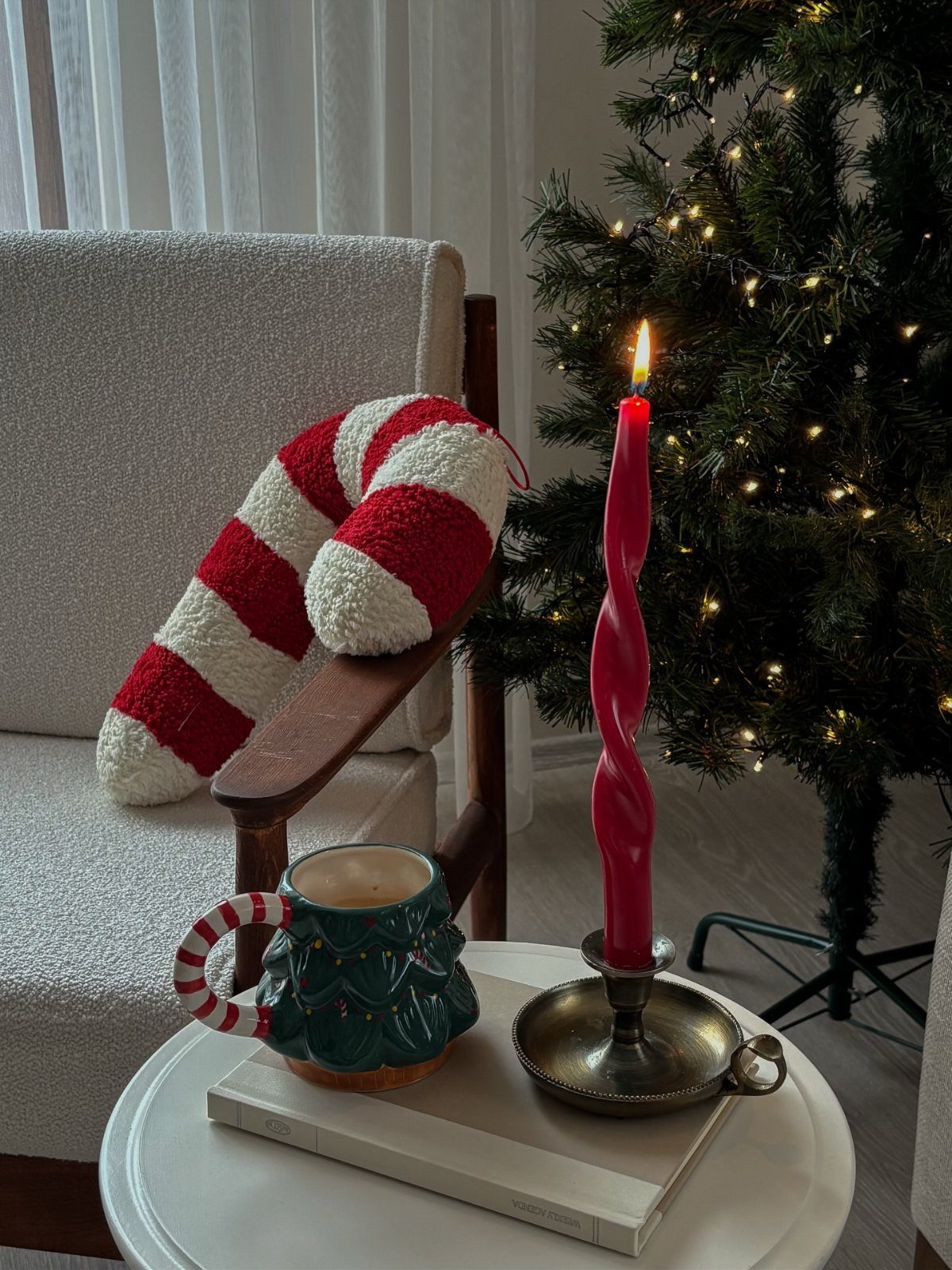 Christmas-themed mug and red spiral candle on a table beside a cozy armchair.
