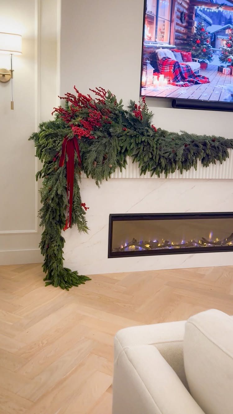 White marble fireplace mantel adorned with a thick green evergreen and red berry garland.