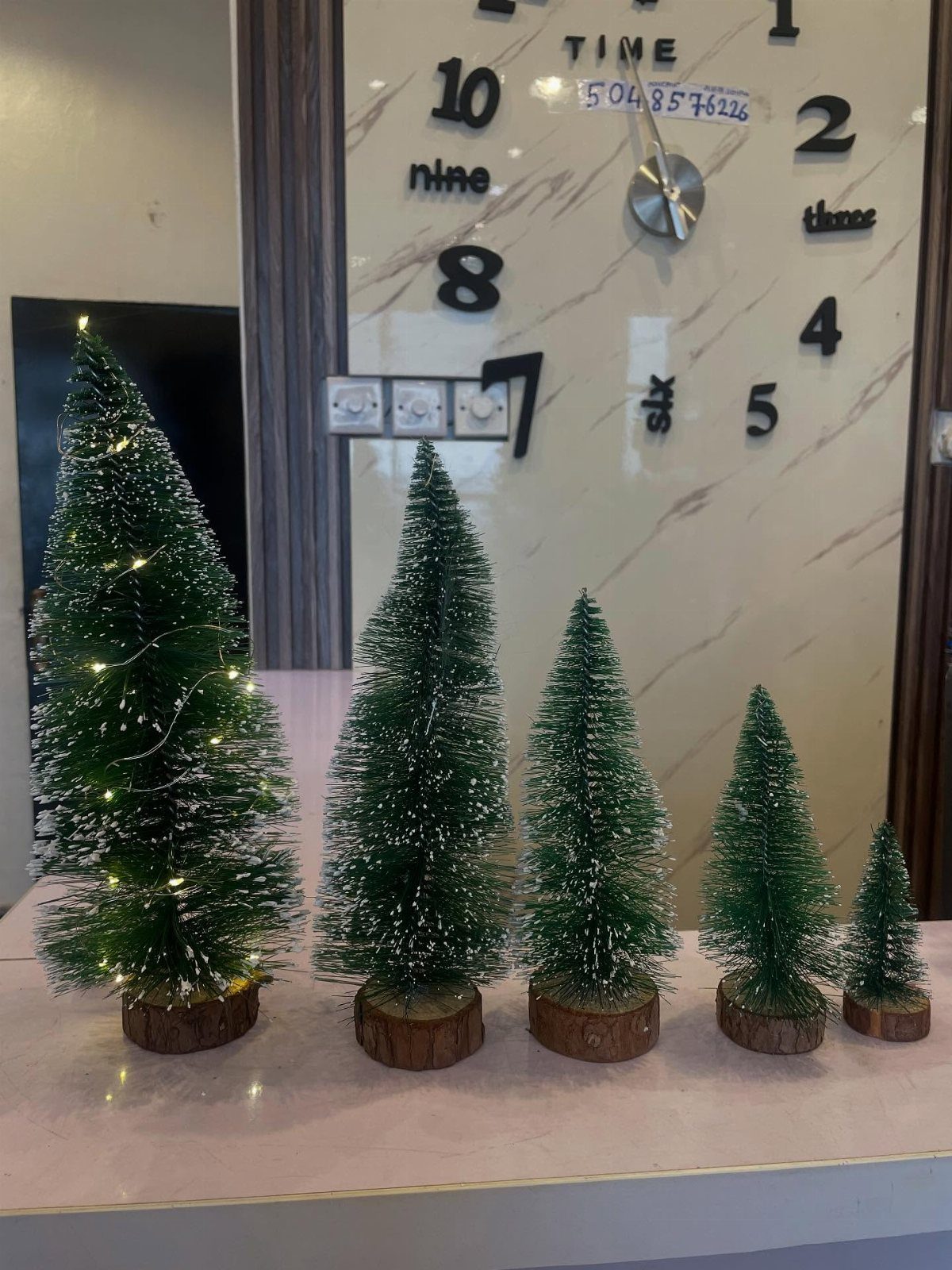 Five small green tabletop Christmas trees of different sizes on wooden bases.