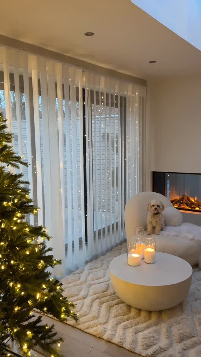 Living room with fairy lights behind sheer curtains, a Christmas tree, and candles.