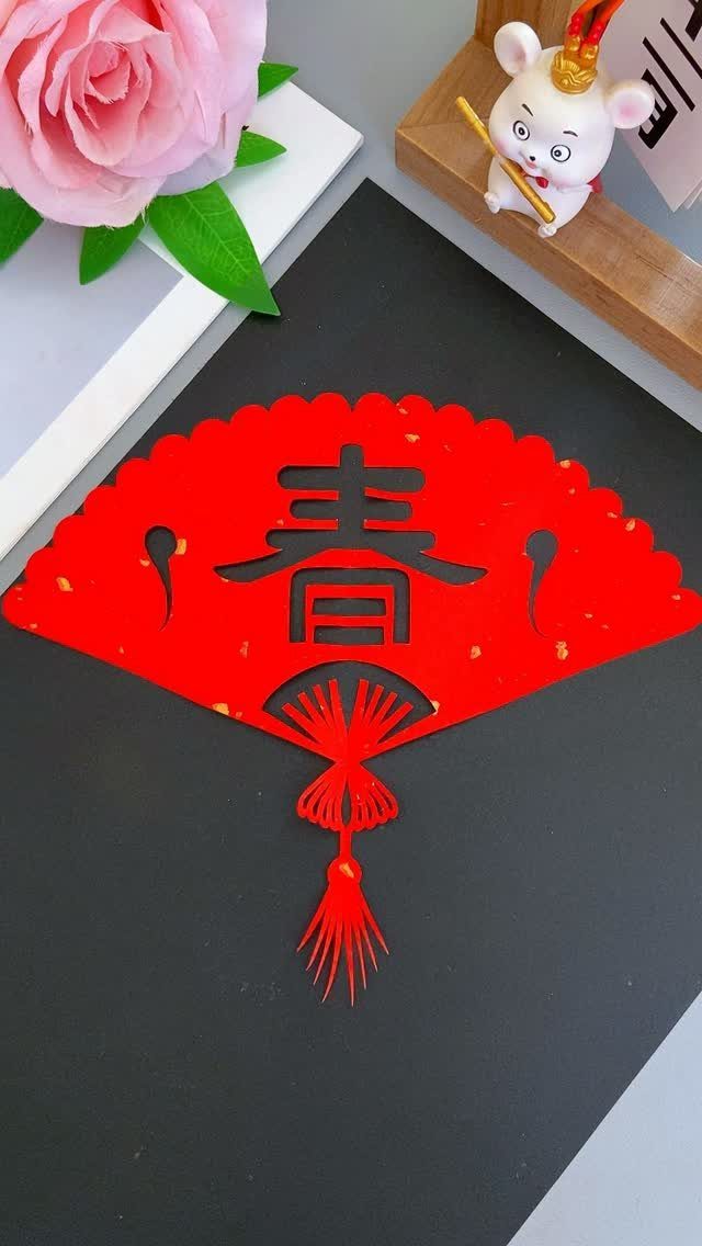 Red decorative paper fan with Chinese character cutout and tassel on black background