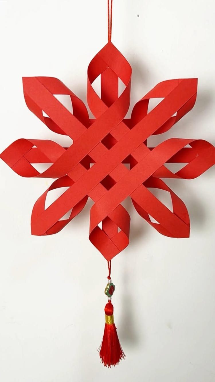 Red paper woven star ornament with a tassel hanging against a white background