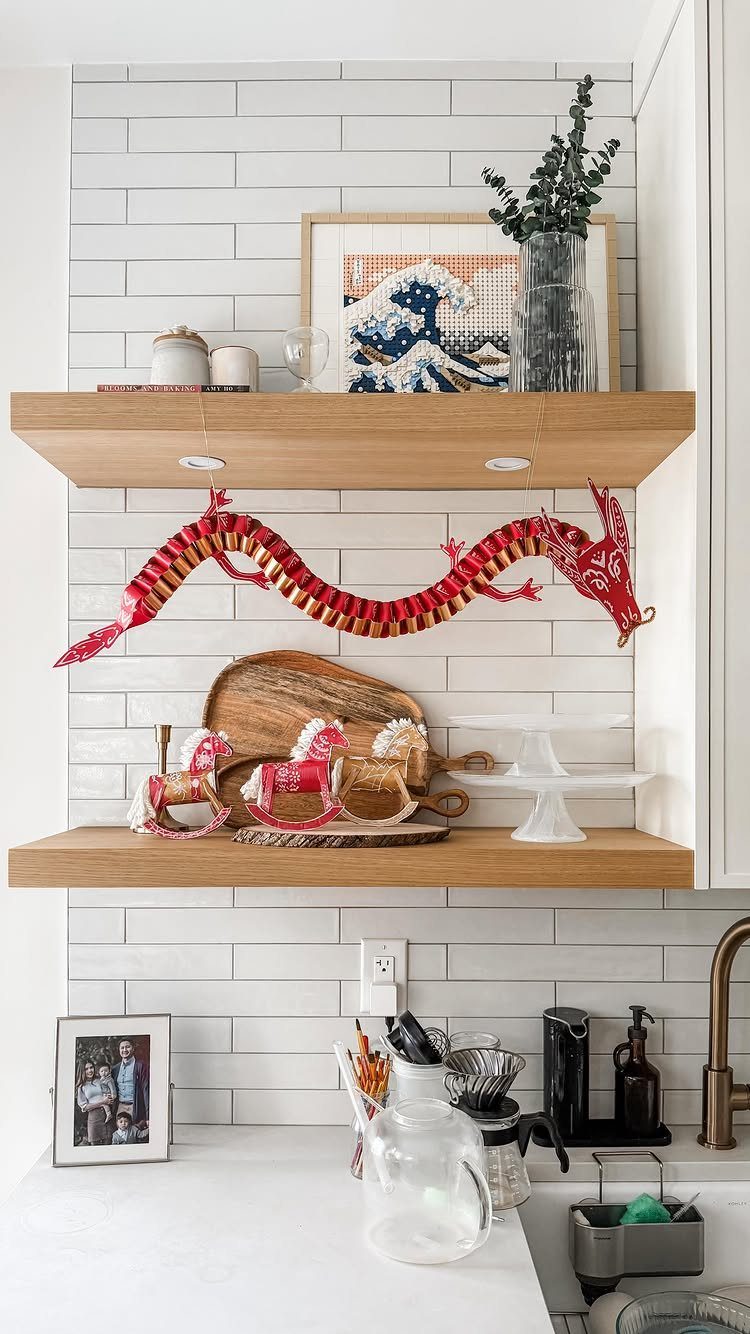 Red and gold Chinese dragon decoration hanging on wooden kitchen shelves against white tiles.