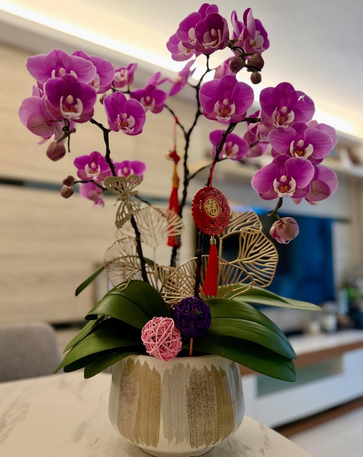 Purple orchids in a white and gold pot with red Lunar New Year ornaments.