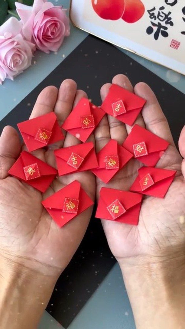 Small red folded envelopes with gold characters held in two open palms.
