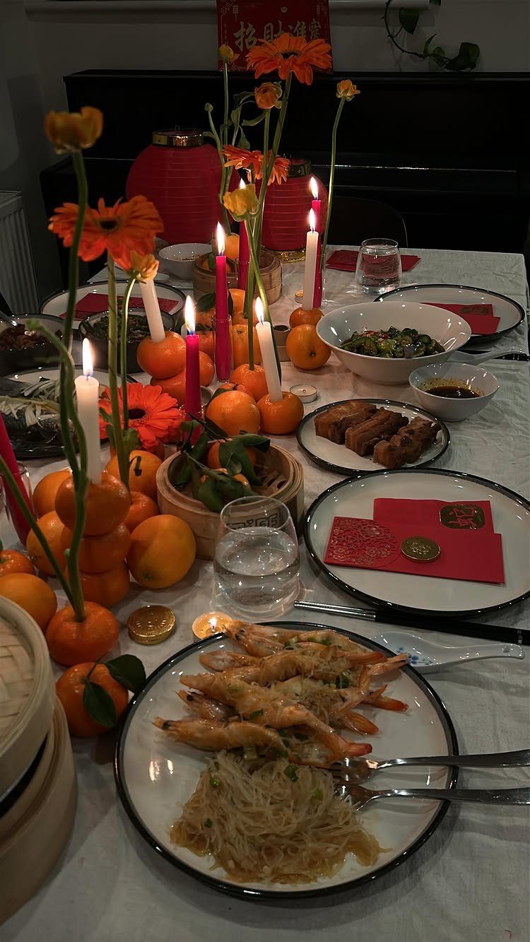 Dining table set with Lunar New Year food, red candles, and orange fruits.